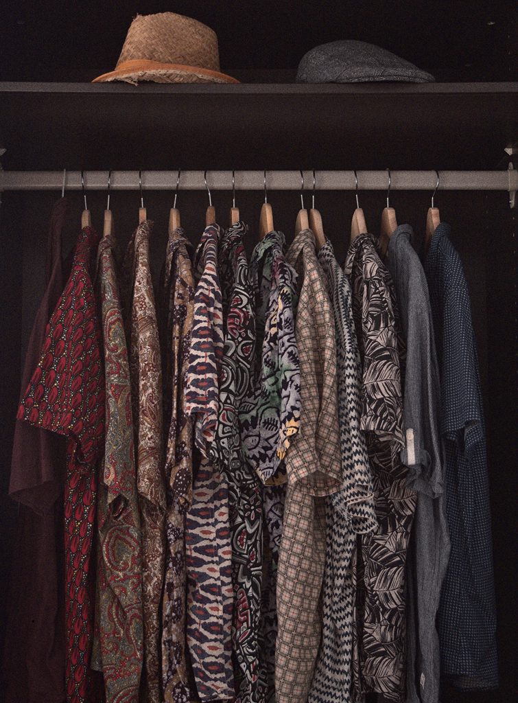 Strohhut und bunte Hemden, die in einem begehbaren Kleiderschrank in einer Second Hand Kleidung Shop in Stuttgart aufbewahrt werden