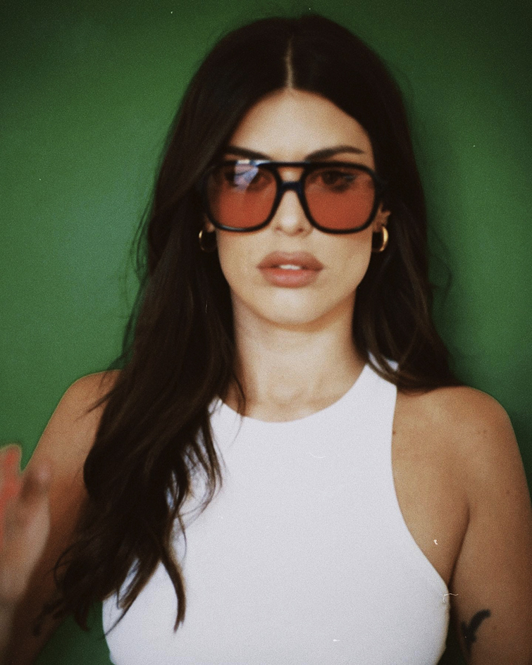 die Weltweit führende Influencerin Aida Domenech vor einem grünen Hintergrund fotografiert, sie trägt eine Sonnenbrille