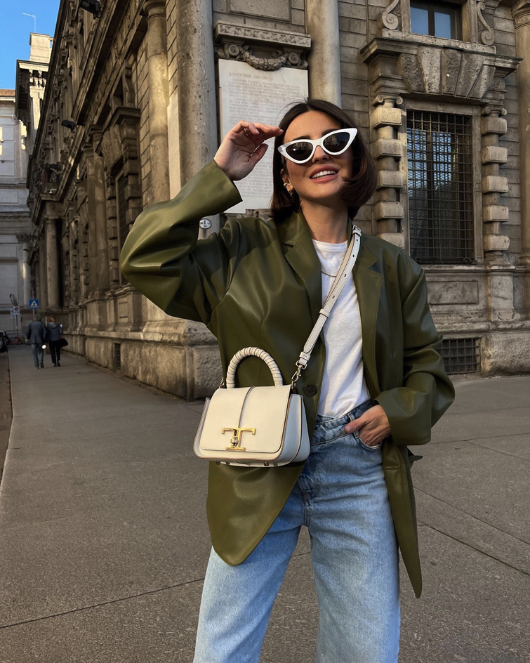 eine der wichtigste weltweite Influencerinnen: Alexandra Pereira die eine weiße Sonnenbrille, grüne Jacke, Jeans und eine beigefarbene Tasche trägt