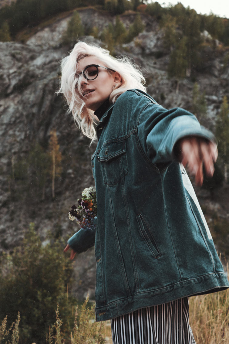 blonde Frau, die eine Jeansjacke, eine gestreifte Hose und Sonnenbrille trägt in der Natur