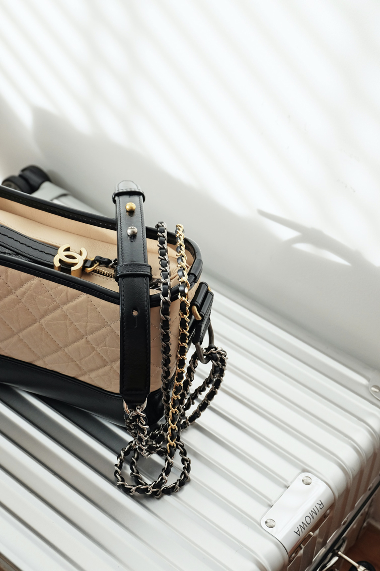 Beige und schwarze Luxushandtasche der Marke Chanel, die auf einem silbernen Koffer liegt 