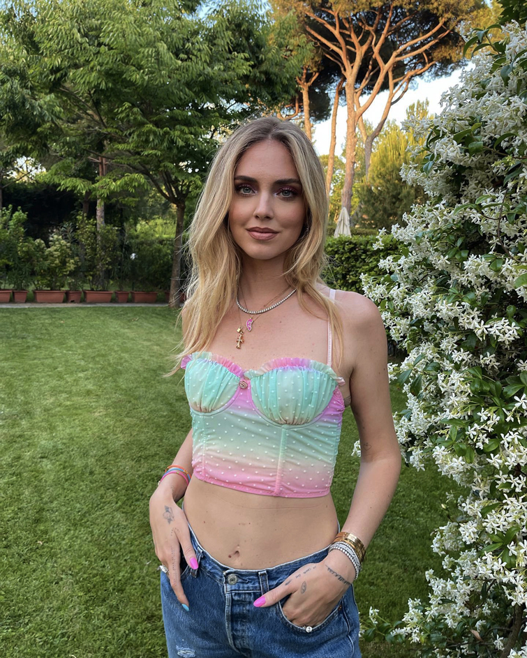 Foto von Chiara Ferragni, einer der weltweit bekannteste Instagram Mode Influencer. Sie trägt eine Jeans und ein mehrfarbiges Top draußen in einem Garten 