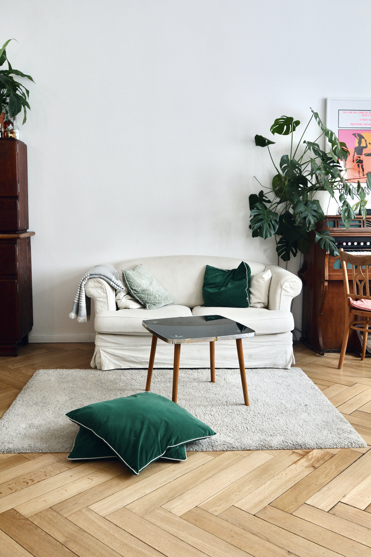 Wohnzimmer mit weißem Sofa und grünen Kissen, eine grüne Pflanze auf einem Klavier stehend. Der perfekte Ort, um eine Kleidertauschparty mit Freunden zu organisieren